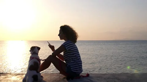 Girl with Dog Using Mobile Phone at Sunset Sea Видео 49366245