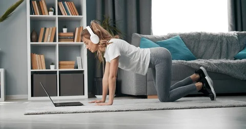 Girl doing exercises while watching tutorial on laptop Vídeos de archivo 128618069