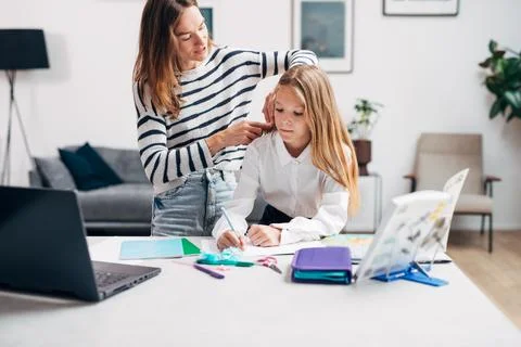 Girl is doing her homework while her mother brushes her hair Stockfoto's