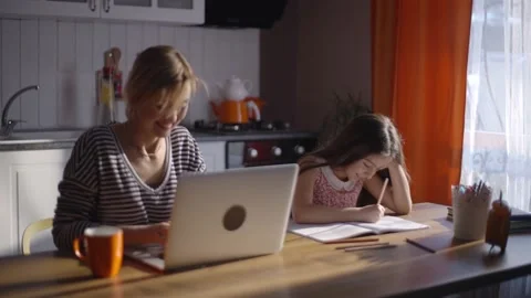 Girl is doing her lessons while mom is working on the computer in the kitchen. Stock Footage 148967832