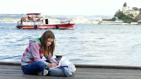 The girl is doing homework on the quay near the sea. Video stock 88409058