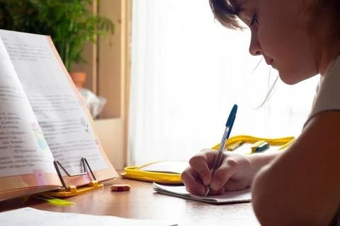 Girl doing homework while sitting at a table near the window in natural light Stock Photos