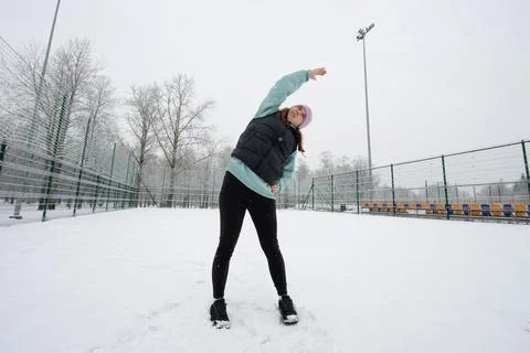 Girl doing a side bend exercise with her arm raised on a snowy sports field.. Stock Photos
