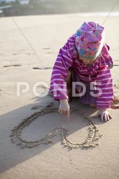 Girl drawing a heart in sand Stock Photos