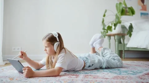Girl drawing on tablet while lying on carpet Stock Footage 312288514