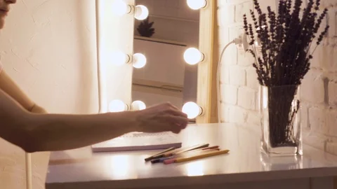 Girl draws in a notebook. In the background lights, make-up mirror. Brick wall Stock Footage 101289946