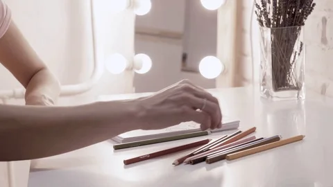 Girl draws in a notebook. In the background lights, make-up mirror. Brick wall Stock Footage 101290053