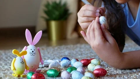 A girl draws a pattern on an Easter egg next to an egg in the shape of a rabbit Stock Footage 176288122
