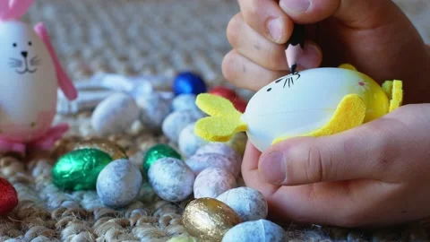 A girl draws a pattern on an Easter egg in the form of a rabbit with Easter eggs Stock Footage 176294703