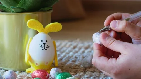 Girl draws a pattern on an Easter egg next to an egg in the shape of a rabbit Stock Footage 176295852