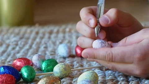 A girl draws a pattern on an Easter egg with Easter eggs in the background Stock Footage 176296212