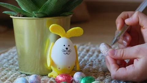 Girl draws a pattern on an Easter egg next to an egg in the shape of a rabbit Stock Footage 176296516