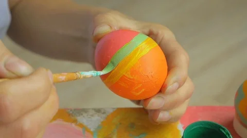 Girl draws a striped pattern on an Easter egg. The hand holds a brush on a Stock Footage 126725737