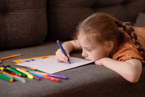 The girl draws while lying on the couch in the living room. The child spends her Stock Photos