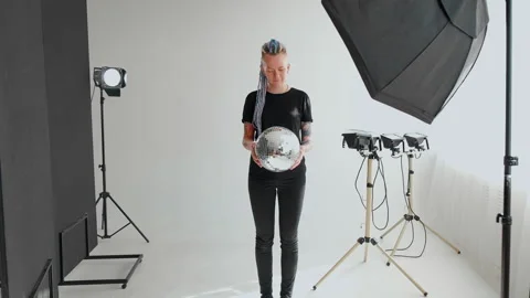 A girl with dreadlocks is standing in a white studio with a disco ball Stock Footage 183981519