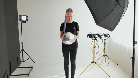 A girl with dreadlocks is standing in a white studio with a disco ball Stock Footage 183982201