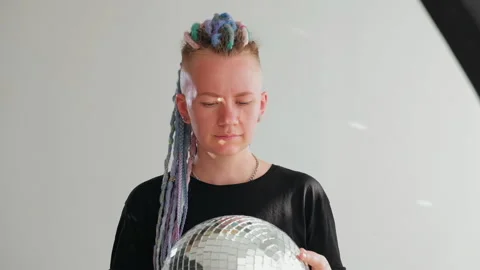 A girl with dreadlocks is standing in a white studio with a disco ball Stock Footage 183998536