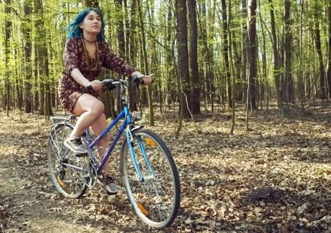 The girl in the dress rides a bicycle through the forest. Stock Photos