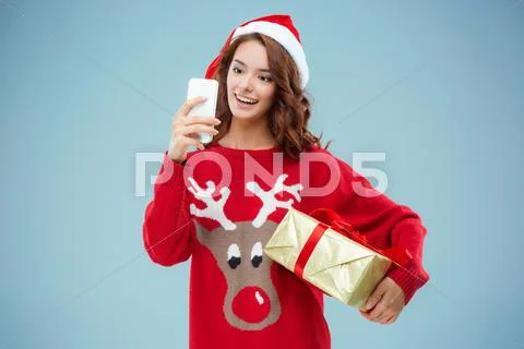 Girl dressed in santa hat with a Christmas gift and phone Stock Photos