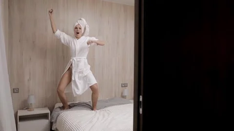 A girl in a dressing gown on the bed, performs the dance of the winner.  Stock Footage 246016884