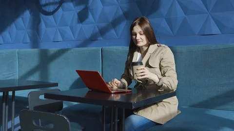 Girl drinking coffee. Surprised looking laptop and comparing information phone Stock Footage 126754200