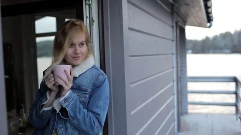 Girl is drinking coffee while sitting on a window of a house on the water Stock Footage 82578460