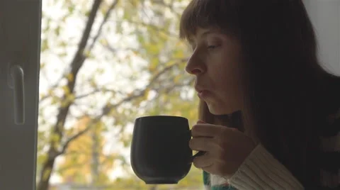 Girl drinking a hot drink , trees with yellow leaves outside the window. Stock Footage 68199518