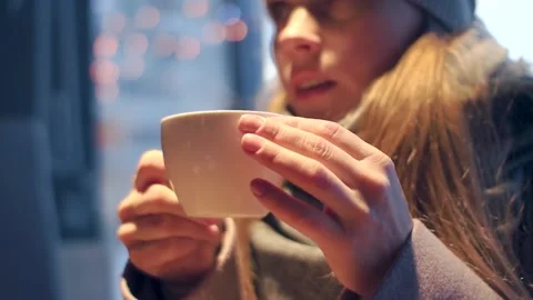 Girl drinking tea from a white mug in a cafe in the light of lamps Stock-Footage 101342389