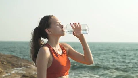 Girl drinks from a bottle while doing sports. fitness exercise at sunset Stock Photos