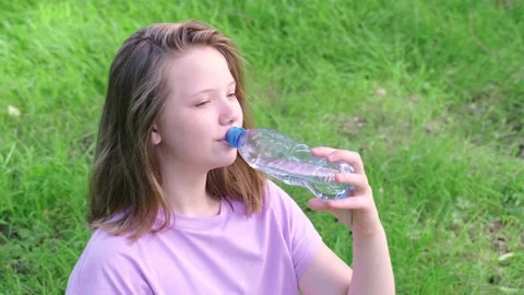 Girl drinks clean drinking water from a bottle in a green city park on a hot Stock Footage 164205660