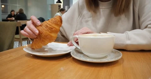 A girl drinks coffee and eats a croissant in a cafe. Vídeo Stock 261117434