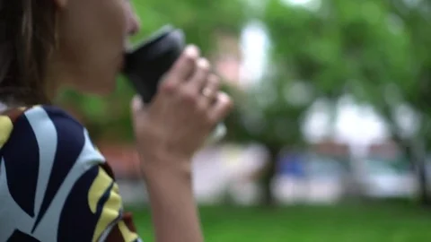 Girl drinks takeaway coffee while walking down the street. Shallow depth of Видео 80130625