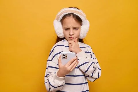 A girl with earmuffs contemplates while using her smartphone, showcasing a .. Stock-Fotos