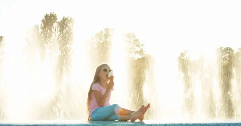 Girl eating ice-cream on fountain background at sunny day Stock Footage