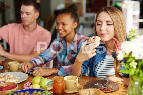Girl eating pastry among her friends by table Stock Photos