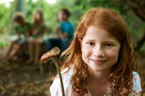 Girl Eating Sausage Cooked On Camp Fire With Friends Stock Photos