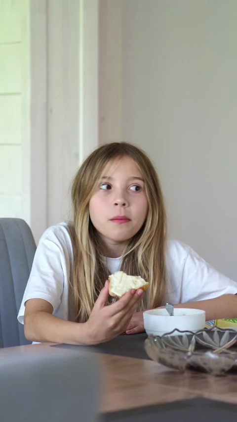 A girl eats a bread and butter for breakfast. A girl with long hair in a white T Stock Footage 311022429