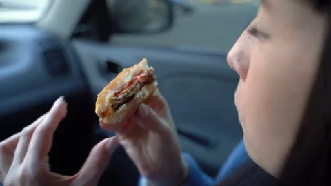 Girl eats a cheeseburger in a car. Slow motion Vidéo 128143614