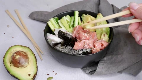 The girl eats red fish and avocado salad. Bowl of rice, cucumber, fish, avocado. Stock Footage 157322601