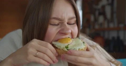 Girl eats sandwich with a poached egg great pleasure chews very actively smiling Stock-Footage 170899758