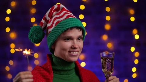 Girl in elf hat hat drinks champagne against the background of Christmas garland Stock Footage 256753174