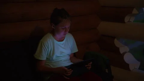 Girl engrossed in digital screen inside rustic wooden cabin at night 스톡 동영상 334161829