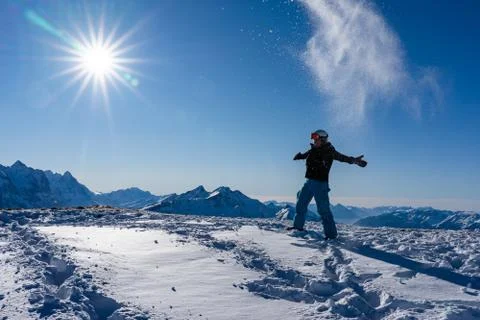 Girl enjoying sunbeams in winter while throwing snow in the air at top of the 스톡 사진