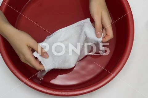 The girl erases a children's white T-shirt in a red basin from stains, cleans Stock Photos