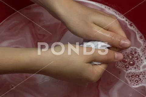 The girl erases a children's white T-shirt in a red basin from stains, cleans Stock Photos