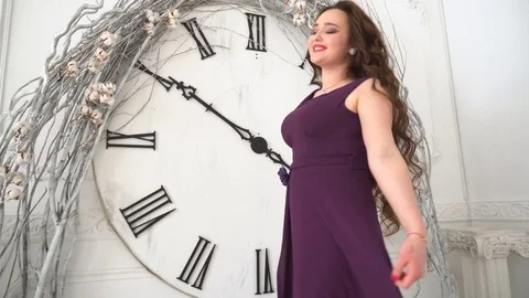 Girl in evening gown smiles on the background big wall clocks Stock Footage