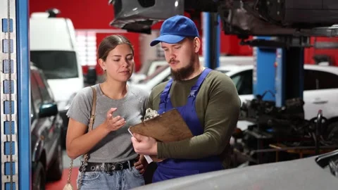 Girl explains the problems of her car to a mechanic. Man writes data on paper Stock Footage 306479944