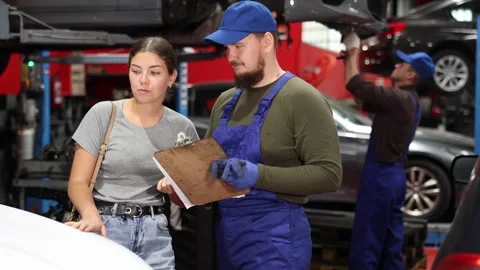 Girl explains the problems of her car to a mechanic. Man writes data on paper Stock Footage 329540653