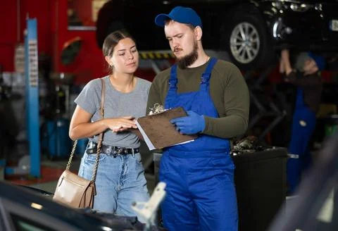 Girl explains the problems of her car to mechanic. Man writes data on paper Stock Photos