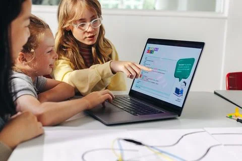 Girl explains robot programming code to classmates on a laptop Photos